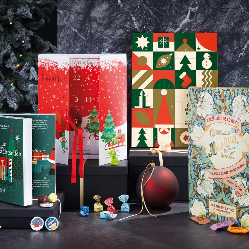 Verschiedene Adventskalender mit festlicher Verpackung und Pralinen, umgeben von Christbaumschmuck.
