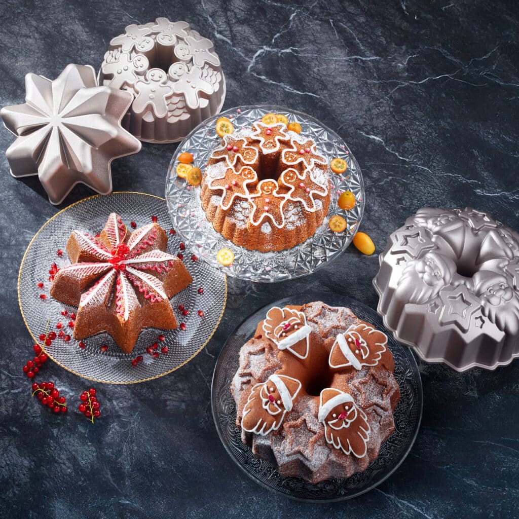 Stern- und Nikolaus-Backformen aus Metall mit passenden weihnachtlich dekorierten Gugelhupfen auf dunklem Marmorhintergrund.