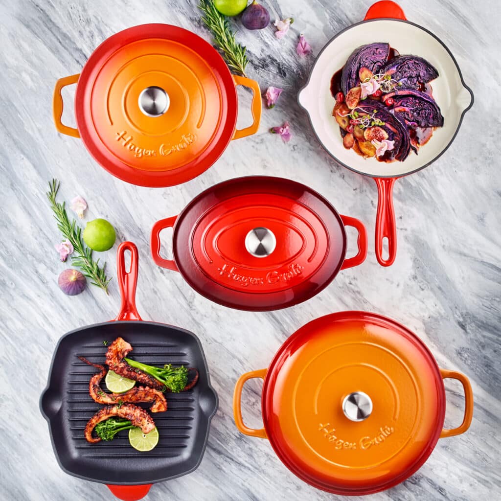 Buntes Set aus emaillierten Gusseisen-Brätern, Pfannen und Grillpfanne mit gebratenem Oktopus und Gemüse.