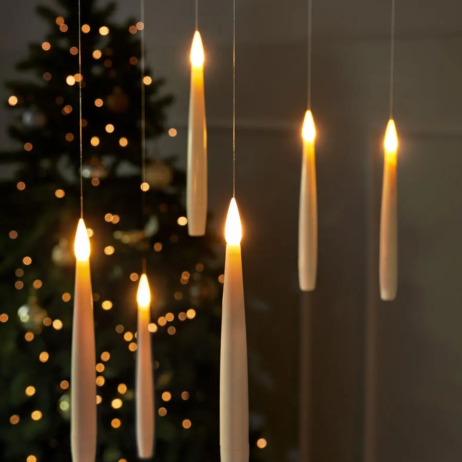 Schwebende LED-Kerzen mit warmem Lichtschein, vor festlich geschmücktem Weihnachtsbaum mit goldenen Kugeln