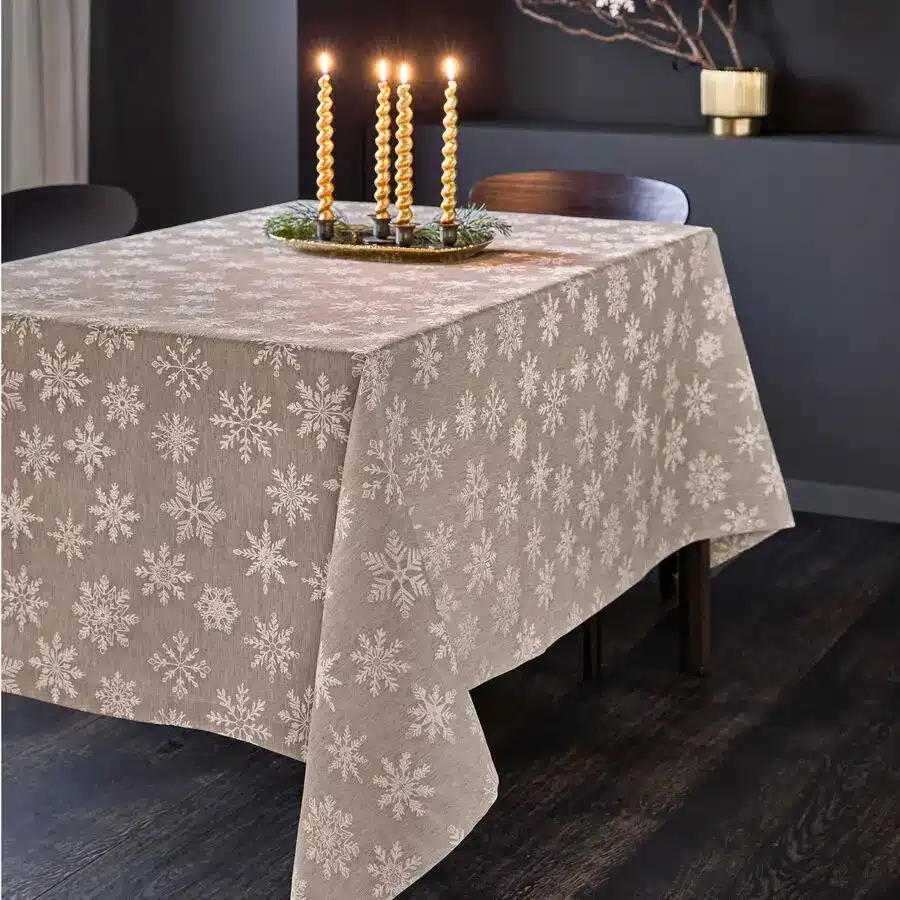 Beige Tischdecke mit weißen Schneeflocken, festlich gedeckt mit goldenen Kerzen