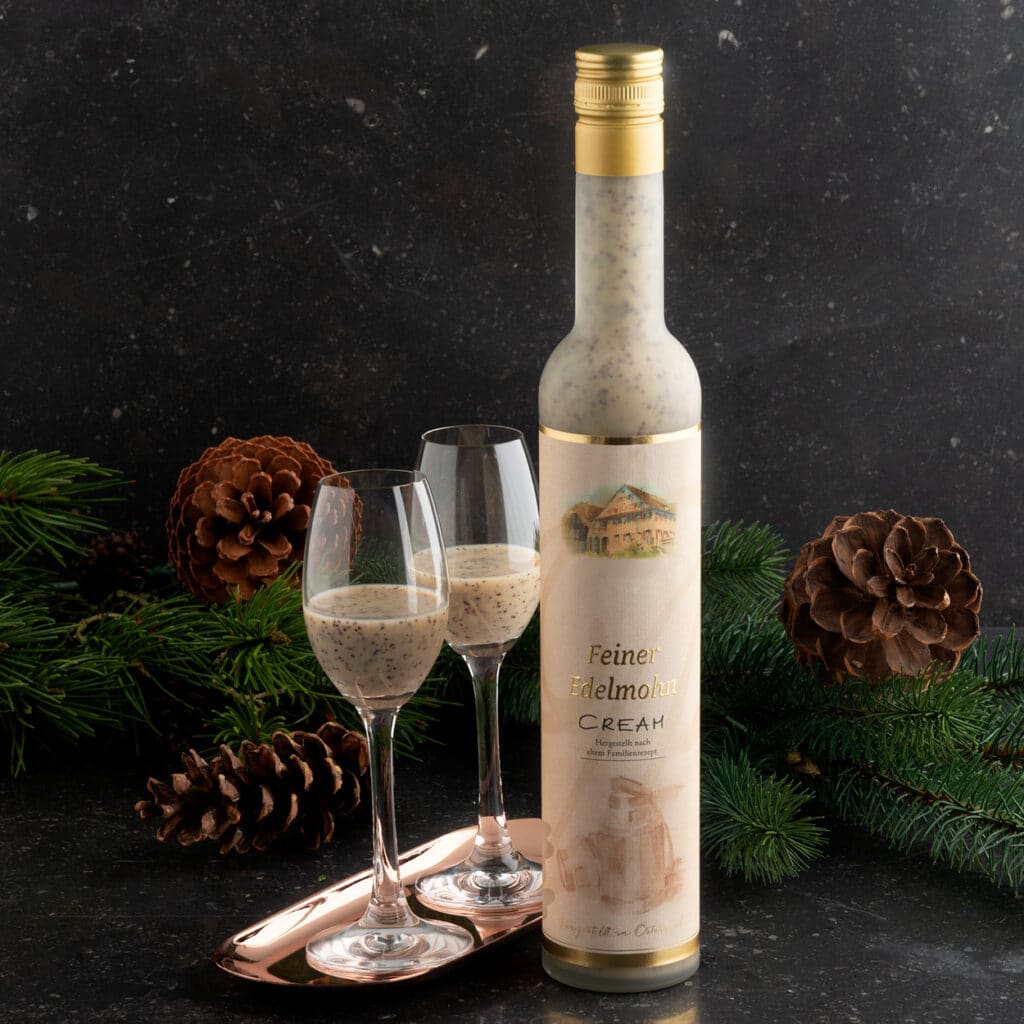 Feiner Edelmohn Cream Likör mit zwei Gläsern, festlich dekoriert mit Tannenzweigen und Zapfen