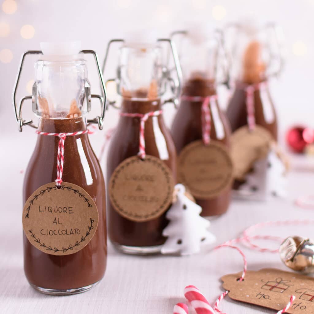 Schokoladenlikör in kleinen Flaschen mit Etiketten und Weihnachtsdeko auf hellem Tisch