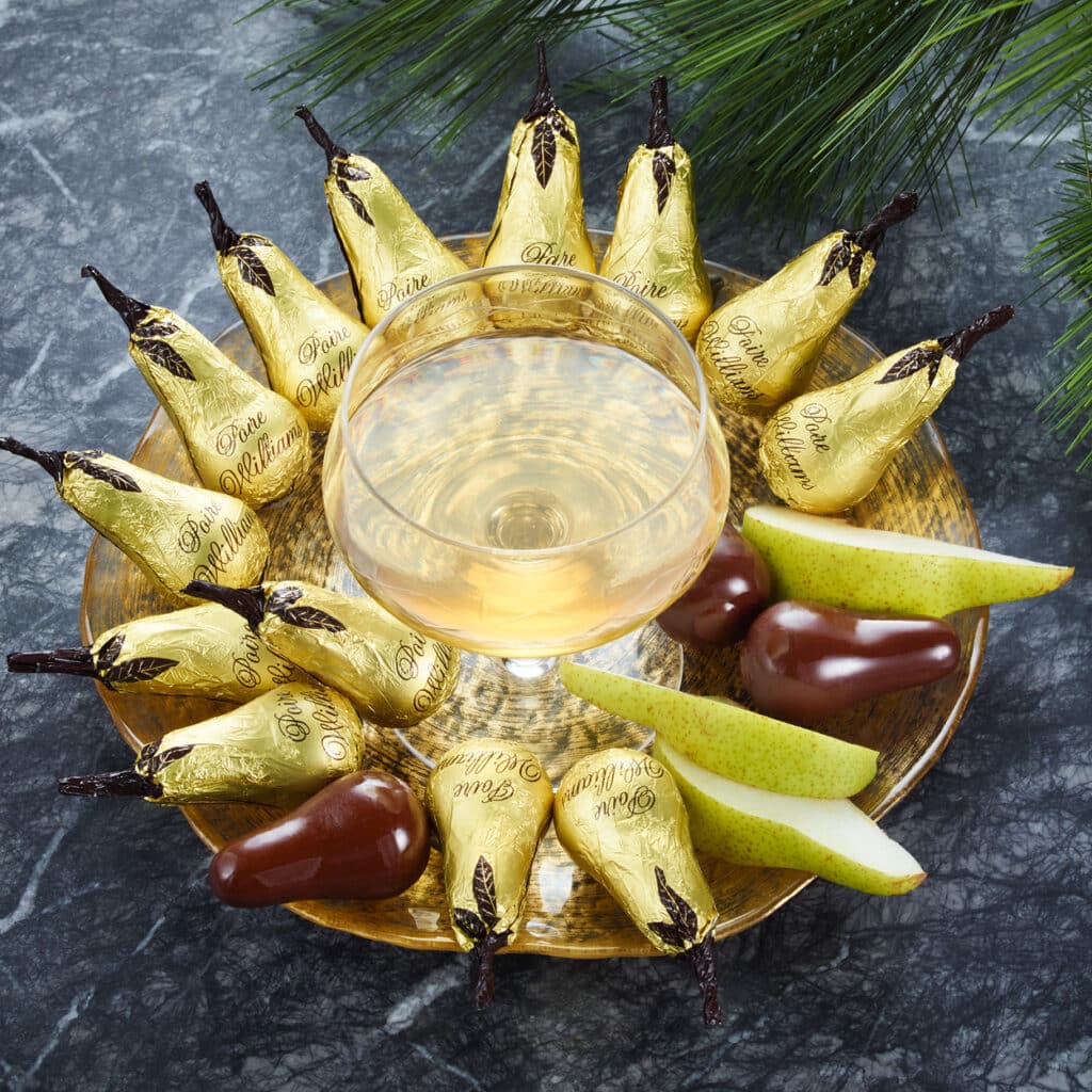 Williamsbirnen mit Schokolade umhüllt, edel verpackt in Goldfolie, serviert mit Glas Obstbrand und frischen Birnenspalten.