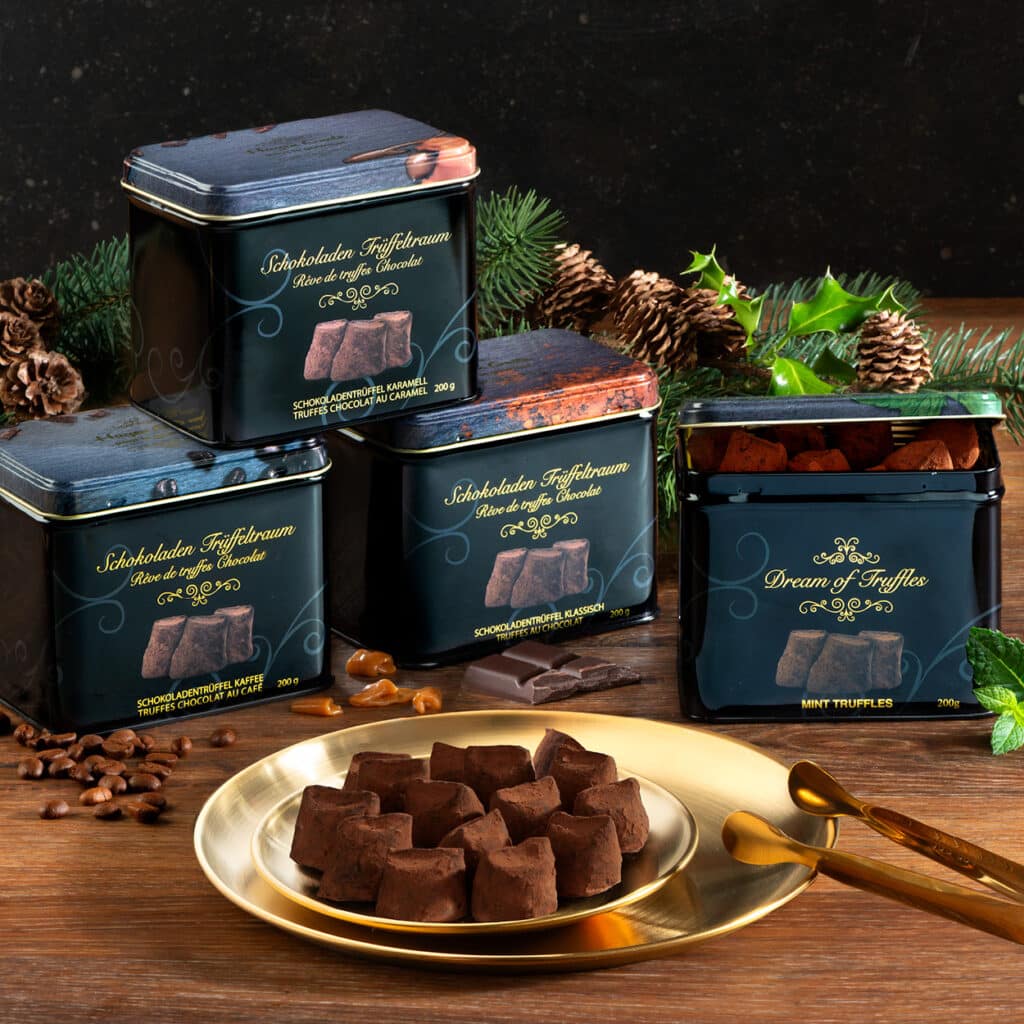Trüffelpralinen in schwarzen Dosen, Sorten Kaffee, Karamell, Klassisch und Minze, dekorativ auf Goldteller serviert.