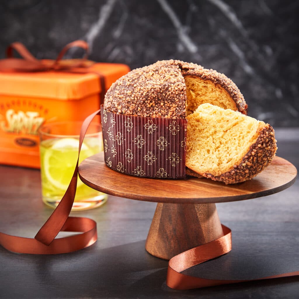 Panettone mit knuspriger Kruste und fluffigem Teig, verpackt in orangefarbener Geschenkbox, angerichtet mit Drink.