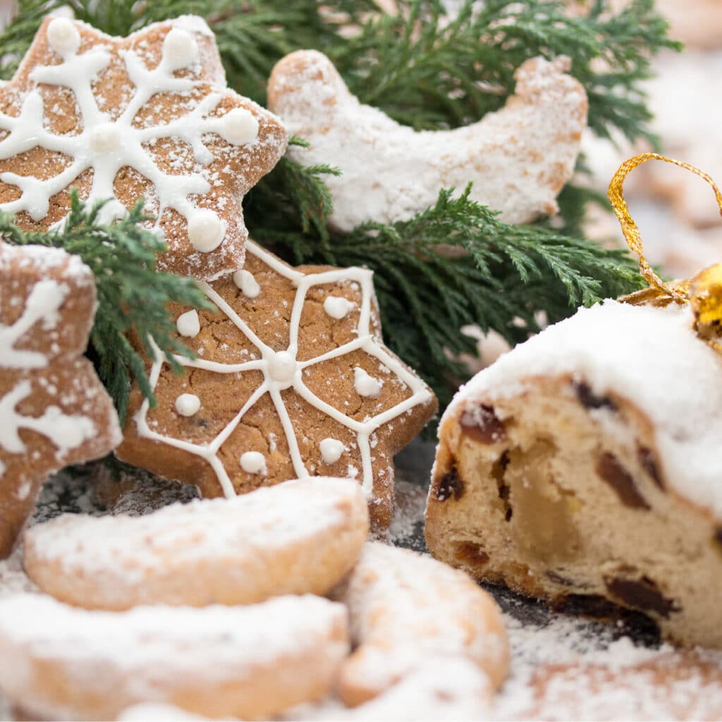Schneeflockenplätzchen mit Zuckerguss und Christstollen im Anschnitt, umrahmt von Tannengrün und weihnachtlicher Deko