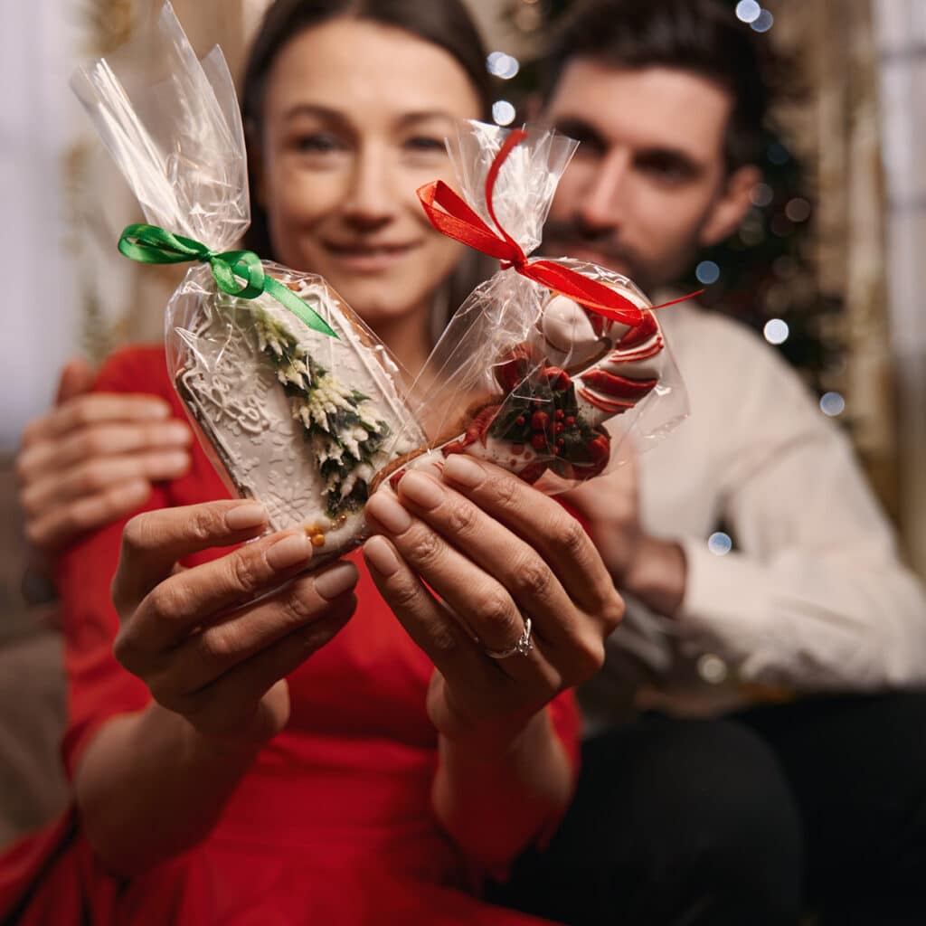 Paar hält verzierte Weihnachtsplätzchen in Geschenkfolie – festliche Kekse mit Tanne und Zuckerstange