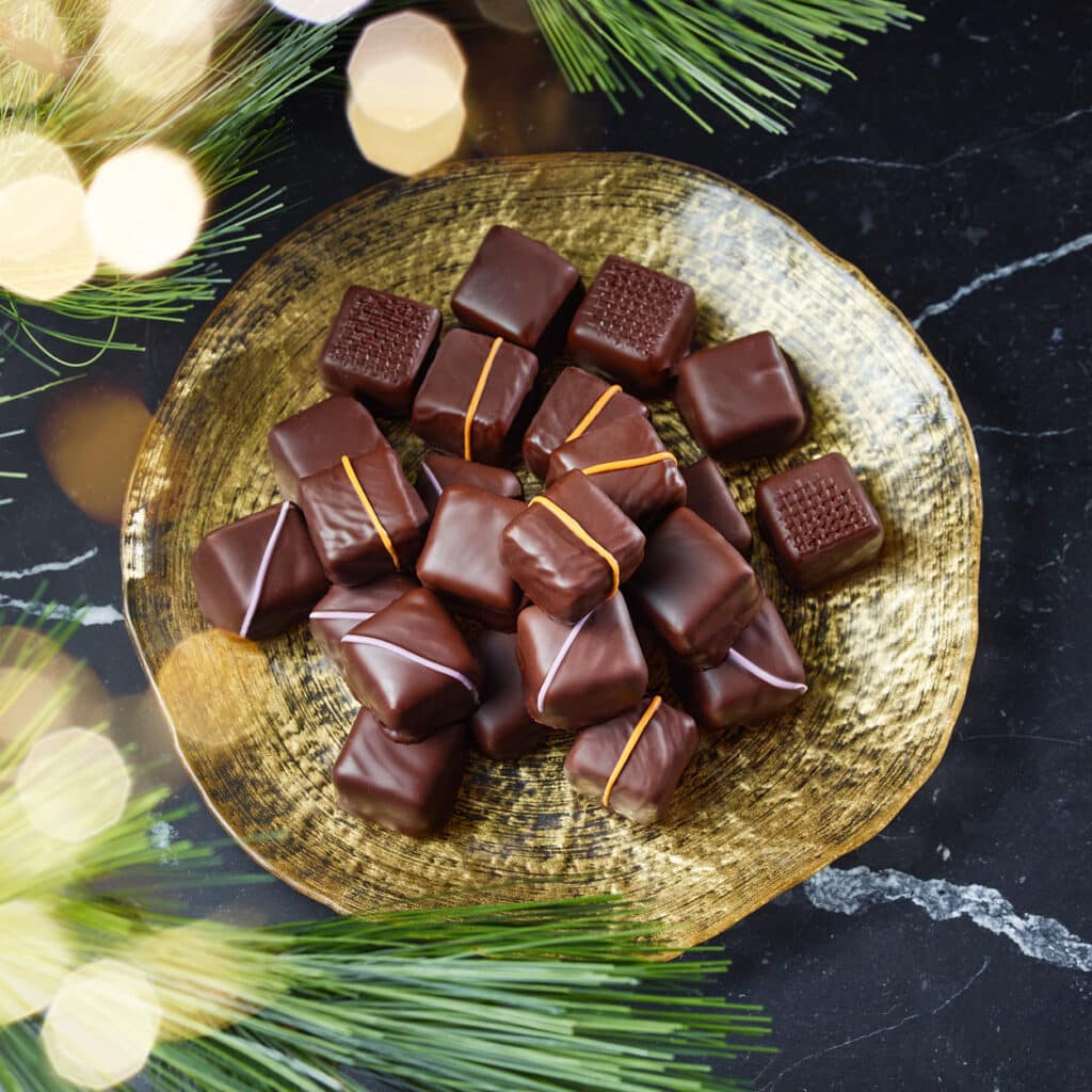 Edle Dominosteine mit feinen Füllungen, angerichtet auf goldener Platte mit weihnachtlicher Tannendeko