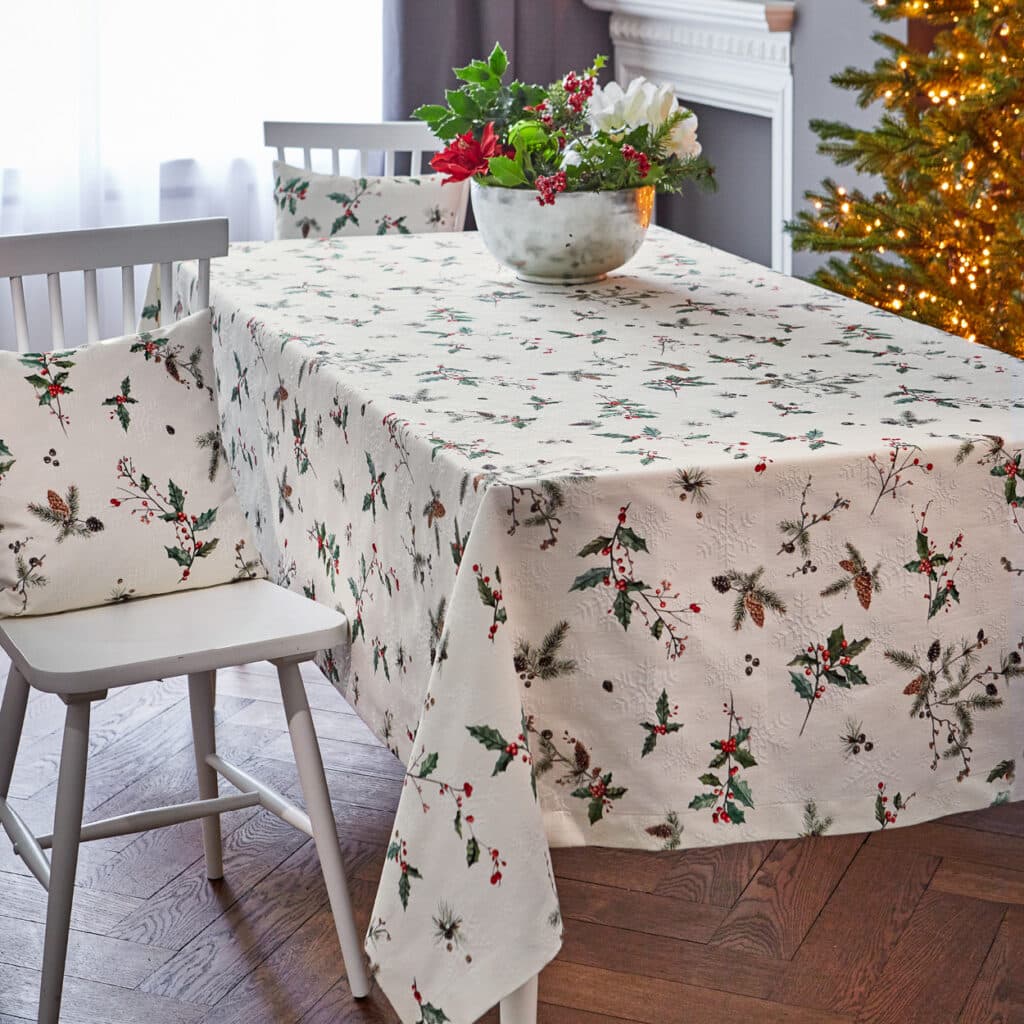 Weiß-cremefarbene Tischdecke mit Stechpalmen- und Zapfenmotiv, weihnachtlich dekoriert