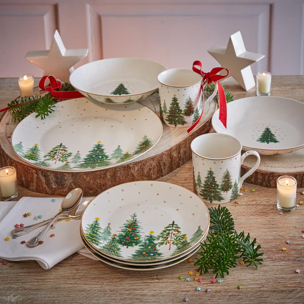 Weißes Weihnachtsgeschirr mit Tannenbaum-Motiv, dekoriert mit Kerzen und Zweigen