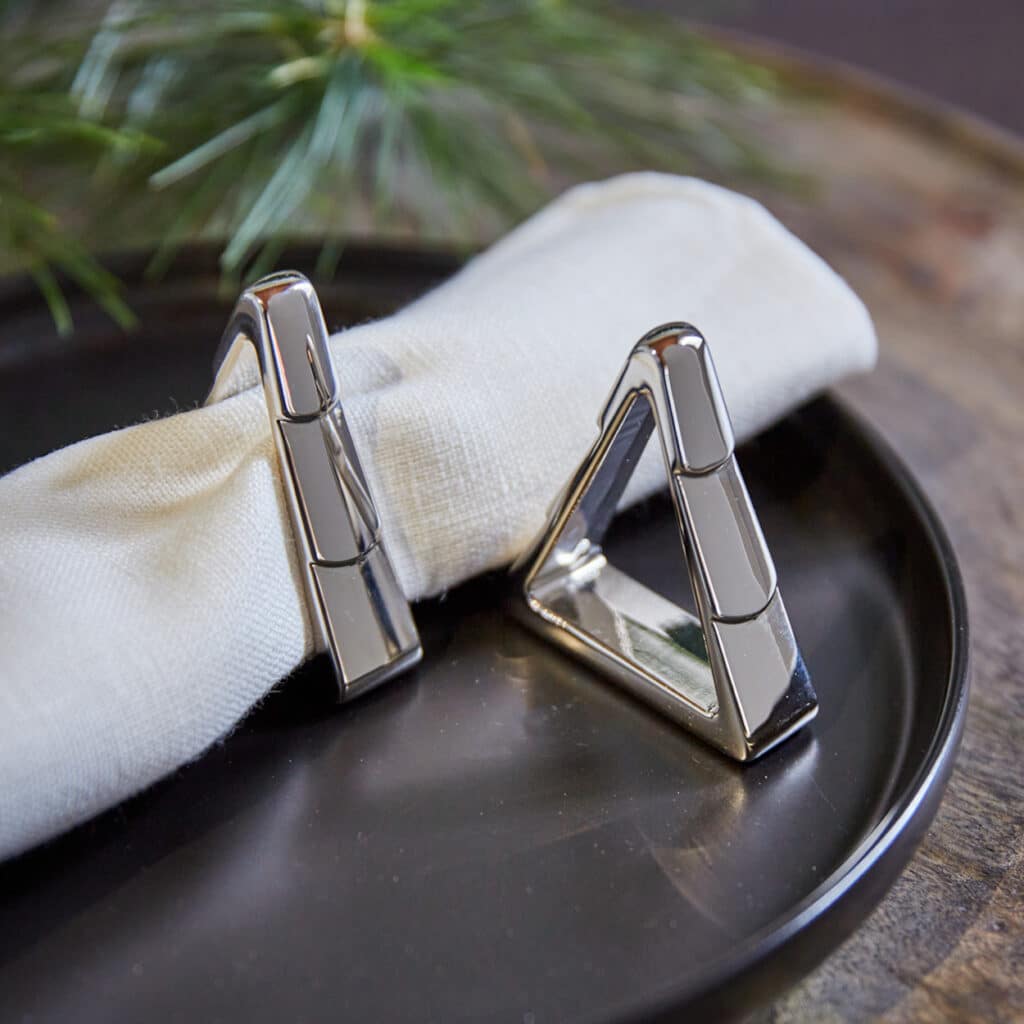 Silberne Serviettenringe in Dreiecksform mit weißer Stoffserviette dekoriert