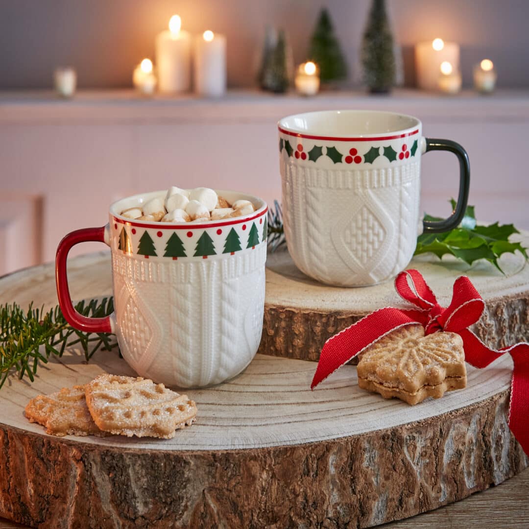 Zwei Weihnachtsbecher mit Kakao, Marshmallows und Plätzchen auf Holzscheiben