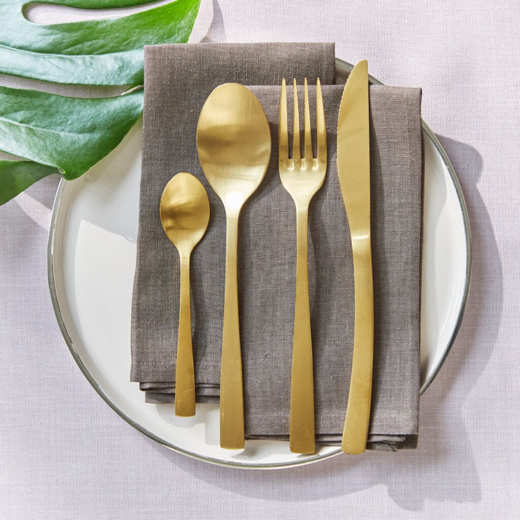 Goldenes Besteck auf grauer Serviette, stilvoll angerichtet auf weißem Teller