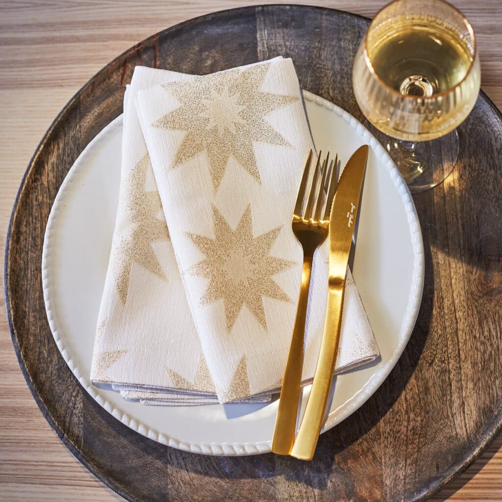Weißer Teller mit goldener Stern-Serviette, goldenem Besteck und Glas Sekt