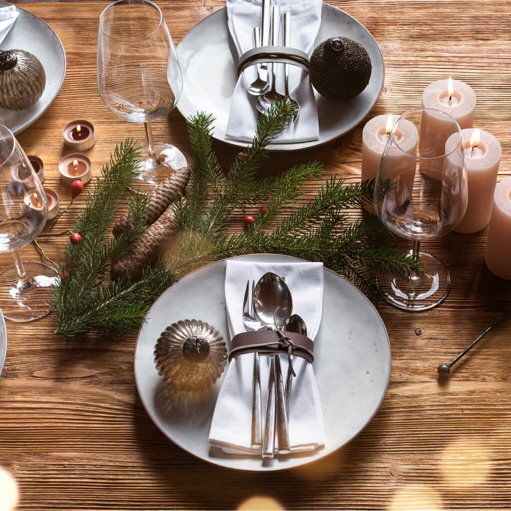 Rustikaler Weihnachtstisch mit weißen Kerzen, Tannenzweigen und festlich gedeckten Tellern