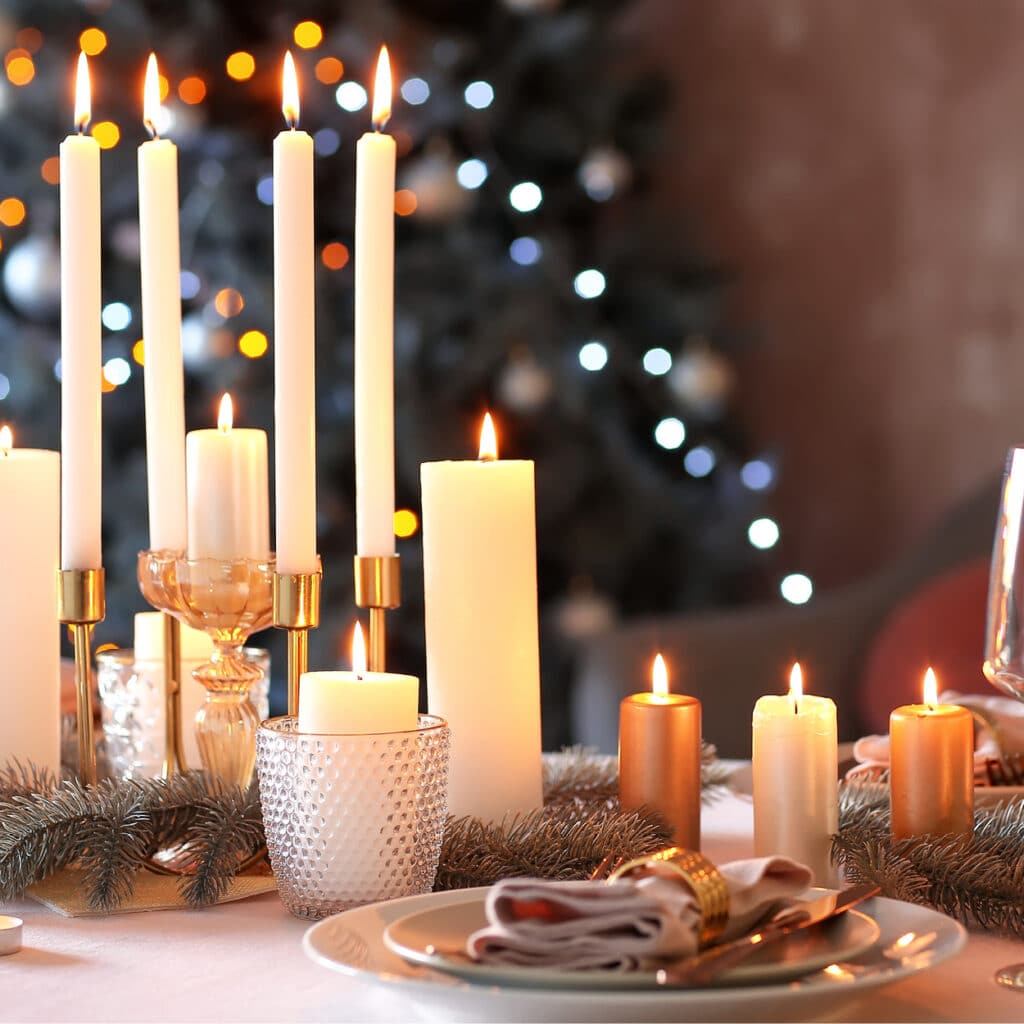Festliche Tischdeko mit weißen Kerzen in Haltern, Tannenzweigen und gedecktem Teller