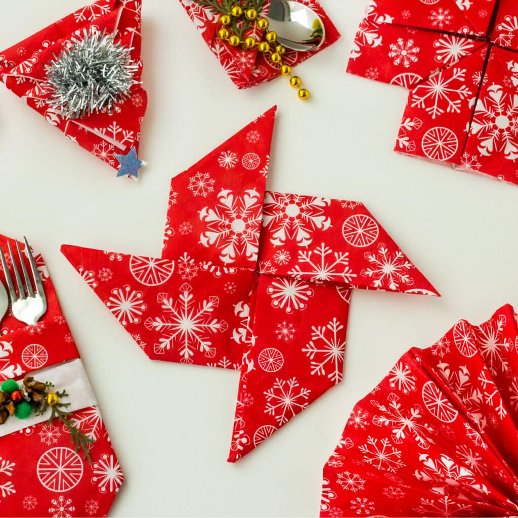 Rote Servietten mit weißen Schneeflockenmotiven, gefaltet als Tischdeko und Origami