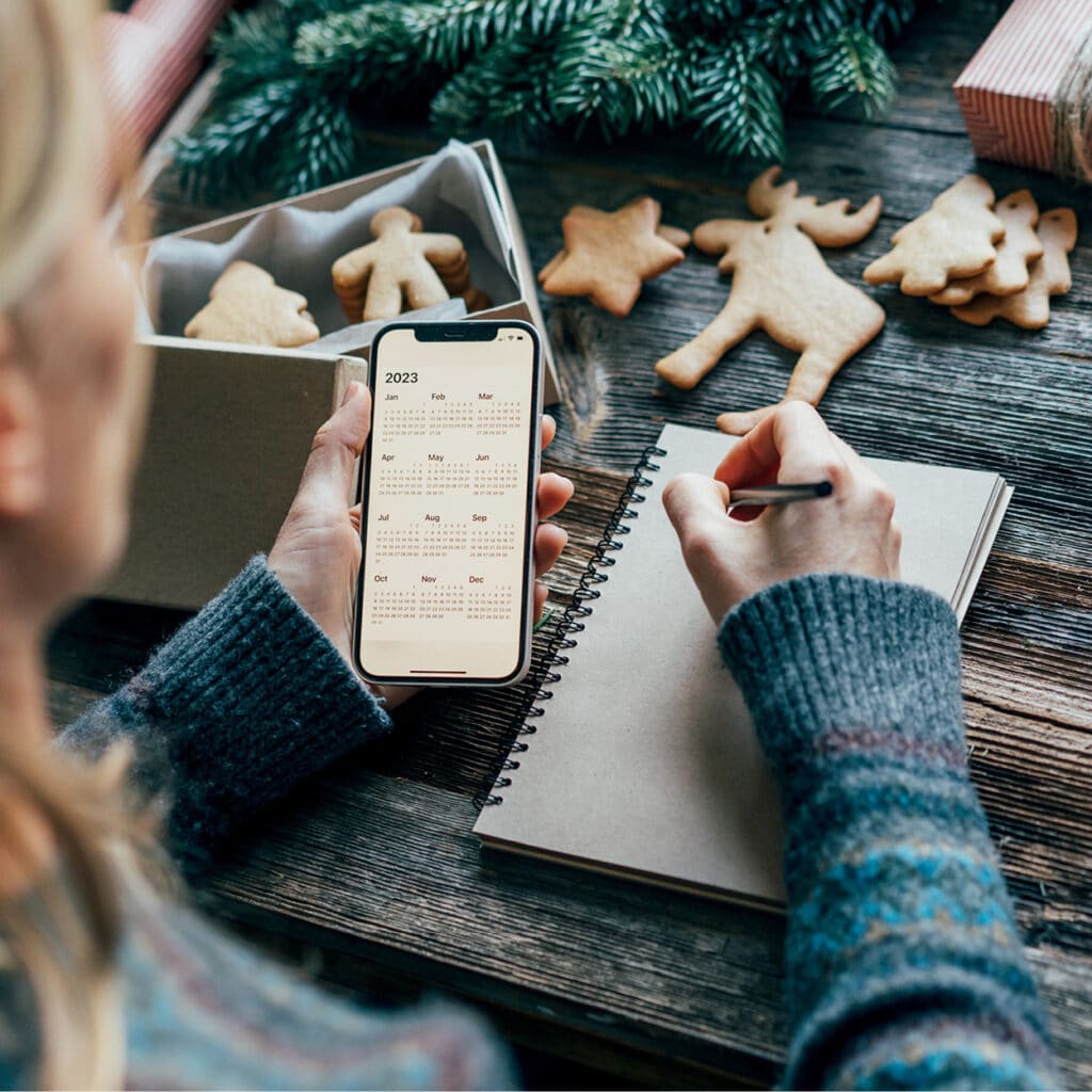 Frau schreibt Notizen, Smartphone zeigt Kalender 2023, Weihnachtsplätzchen daneben
