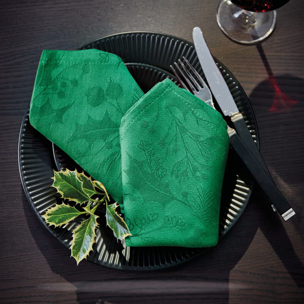 Schwarzer Teller mit grüner Stoffserviette und Ilexzweig, festlich gedeckt