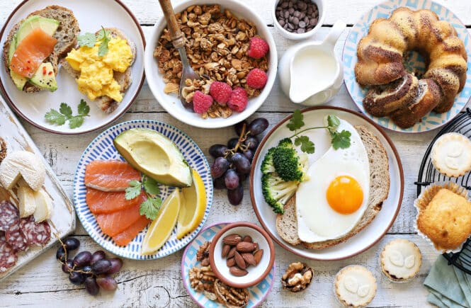 Frühstücks-Spread mit Avocado-Lachs-Brot, Rührei, Spiegelei auf Brot, Müsli mit Himbeeren, Kuchen und Gebäck