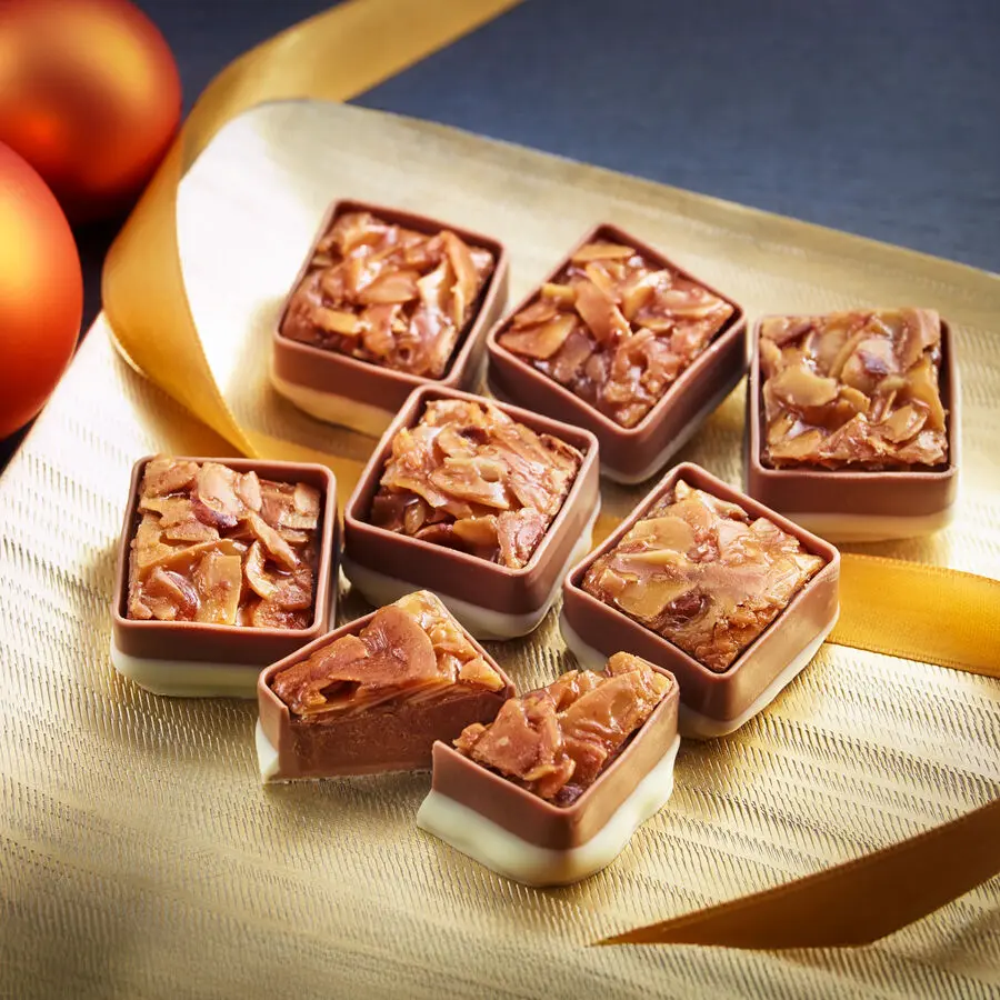 Nahaufnahme von rechteckigen Florentiner-Pralinen mit Mandelkrokant, teilweise halbiert, auf goldenem Untergrund arrangiert.